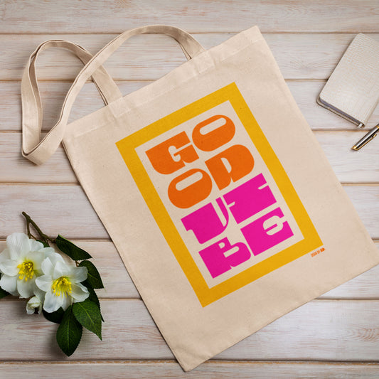 A cotton canvas tote bag with yellow, orange, and pink type showing "Good Vibe."