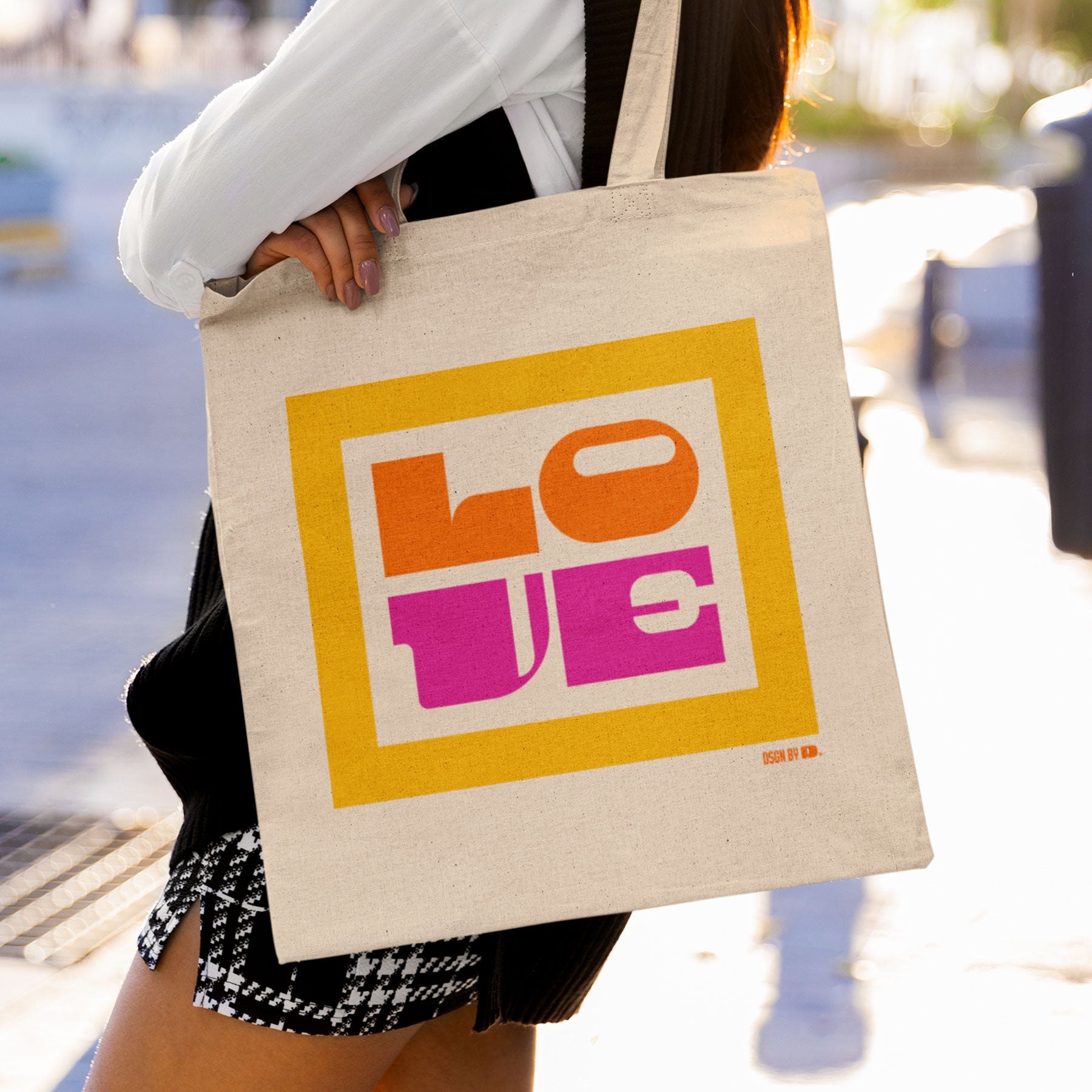 A woman carrying a cotton canvas tote bag with yellow, orange, and pink design.